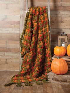 an orange and green blanket sitting on top of a wooden crate next to pumpkins