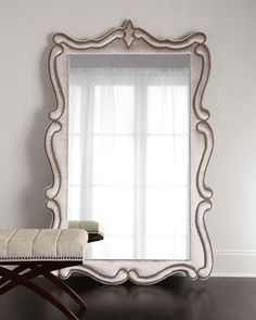 a white mirror sitting on top of a wooden floor next to a chair and window