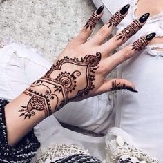 a woman's hand with henna tattoos and black nails on her left arm