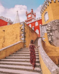 a woman in a red dress is walking up some stairs to a castle like building