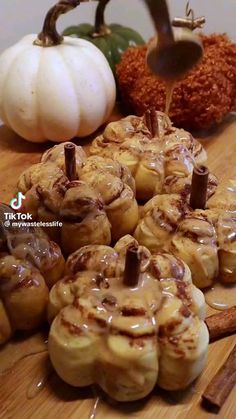 cinnamon rolls with icing on a cutting board next to pumpkins and other autumn decorations