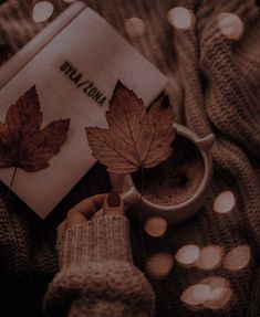 a person is holding a cup of coffee and reading a book with autumn leaves on it