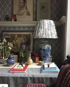 a table topped with books and vases next to a lamp on top of a table