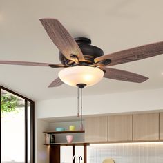 a ceiling fan that is hanging from the ceiling in a room with wooden cabinets and windows