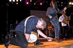 a man kneeling down to pick up a frisbee from the ground on stage