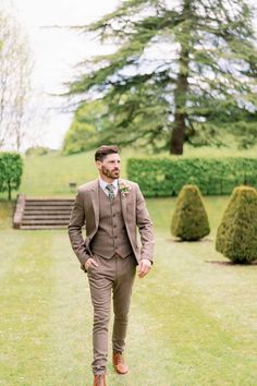 a man in a suit and tie walking through the grass