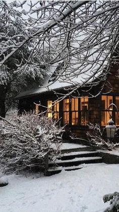 a cabin in the woods is lit up at night, with snow on the ground