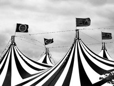 black and white photograph of circus tents with flags in the sky behind them on a cloudy day