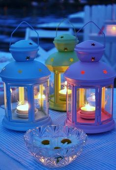 three colorful lanterns sitting on top of a table next to each other with lit candles in them