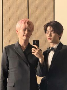 two young men in tuxedos taking a selfie with their cell phone while standing next to each other