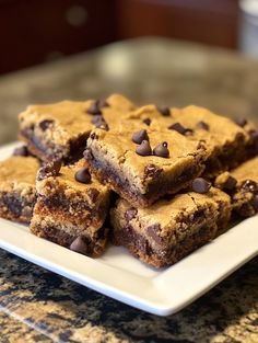 chocolate chip cookie bars stacked on top of each other on a white plate with a glass table in the background