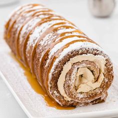 a roll covered in powdered sugar and caramel sauce on a white square plate