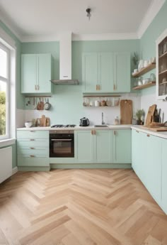 a kitchen with light green cabinets and wood flooring is pictured in this image, there are shelves on the wall above the stove