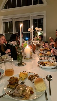 a group of people sitting around a dinner table with food on the plates and candles