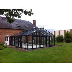 a glass house sitting on top of a lush green field next to a brick building