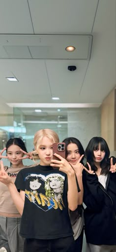 four young women taking pictures with their cell phones in an office building hallway, one holding up her fingers to the camera