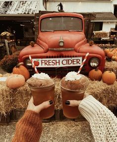 two people holding drinks in front of an old truck and hay bales with pumpkins