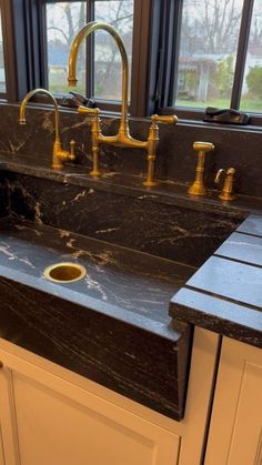 a black marble sink with gold faucets in front of a window