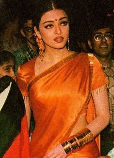 an old photo of a woman in orange sari and gold jewelry standing next to other people