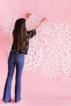 a woman is working on an intricate paper wall decoration with white flowers and leaves, against a pink background