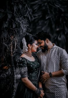 a man and woman standing next to each other in front of some trees with leaves