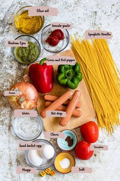 ingredients to make pasta laid out on a cutting board, including tomatoes, peppers, onions, and garlic