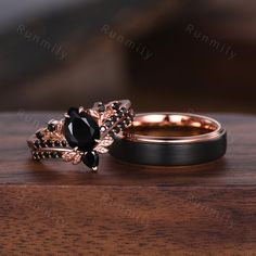 two wedding rings with black stones on top of each other sitting on a wooden table