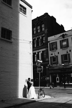 a bride and groom standing next to a stop sign in front of some tall buildings