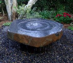 a large rock sitting on top of a gravel ground next to a tree and bushes