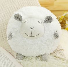 a white sheep stuffed animal sitting on top of a bed next to a book and flowers