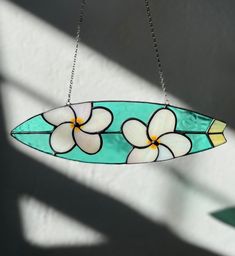 a stained glass surfboard with white flowers hanging from it's side on a chain