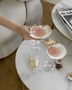 a person holding two wine glasses with seashells in them on a white table