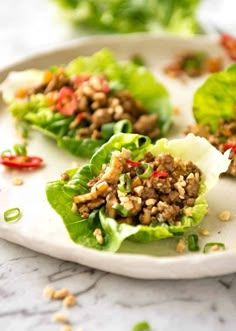 lettuce wraps filled with meat and seasoning on a white plate, ready to be eaten