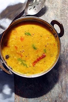 a pot filled with soup sitting on top of a table next to a spoon and napkin