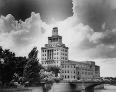 an old photo of a large building with a bridge in the foreground and clouds in the background