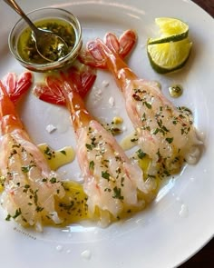 a white plate topped with shrimp next to lemon wedges and olive oil on a wooden table