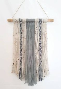 a macrame hanging on a white wall with some wood and yarn attached to it