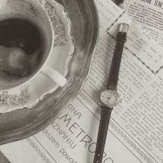 a cup of tea and a watch sitting on top of a newspaper next to it