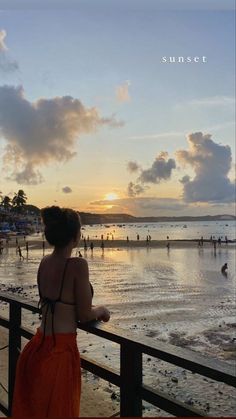 a woman looking out over the beach at sunset with people in the water and onlookers