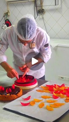 a chef is decorating a cake with red flowers on the table and orange petals scattered around it