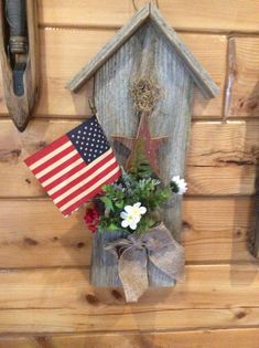 an american flag hanging on the side of a wooden house with flowers in front of it