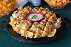 a waffle with cheese, bacon and ranch dressing on it sits in front of some chips