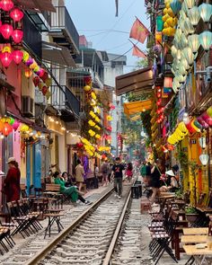 people are sitting at tables on the tracks in an alleyway with lanterns hanging above them