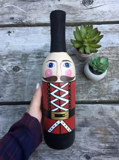 a hand holding a bottle with a nutcracker painted on it and a succulent plant in the background