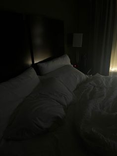 an unmade bed in a dark room with light coming from the window behind it