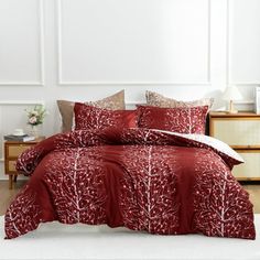 a bed with red comforters and pillows in a room next to a dresser,