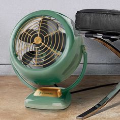 a green fan sitting on top of a table next to a black chair