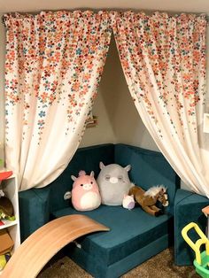 a couch with two stuffed animals on it in front of a curtained window and bookshelf