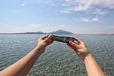 two hands holding something over the water with mountains in the backgrouds behind them