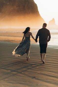 a man and woman walking on the beach holding hands